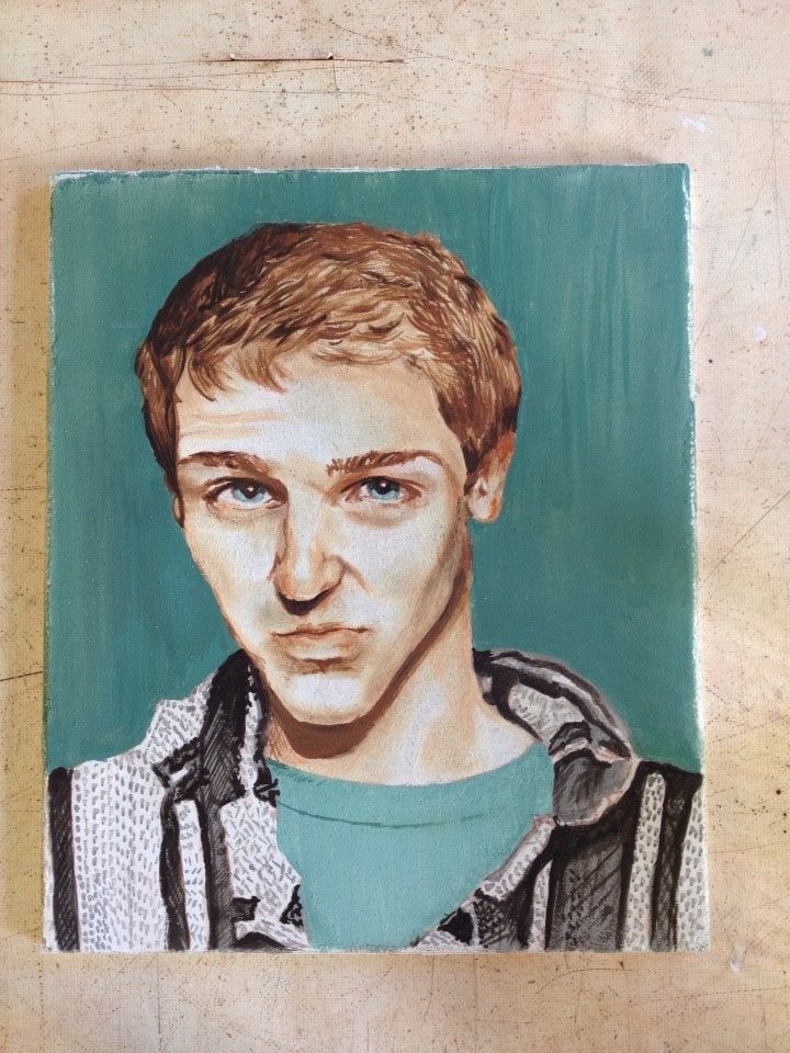 Portrait of a young man with reddish-blond hair wearing a striped hoodie against a teal background.