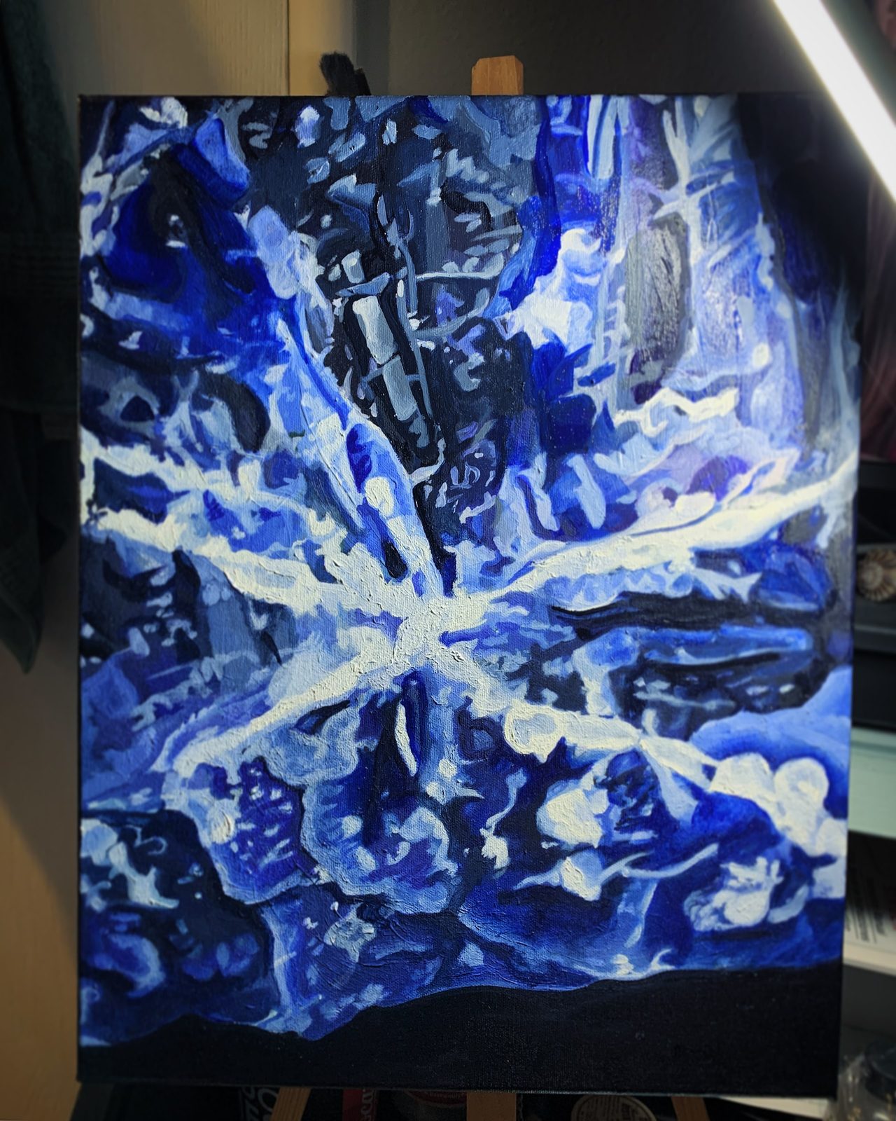 Abstract painting of white swirling burst forms against a dark blue background, shown on an easel.
