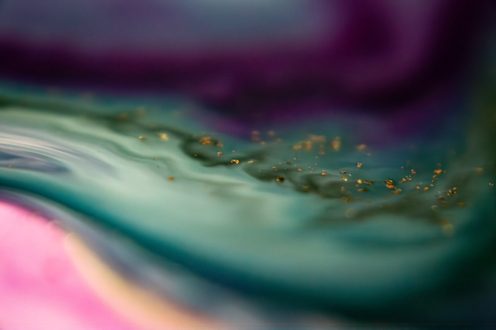 Purple and pink fading into teal, with a scatter of gold flecks along the diffusion line.