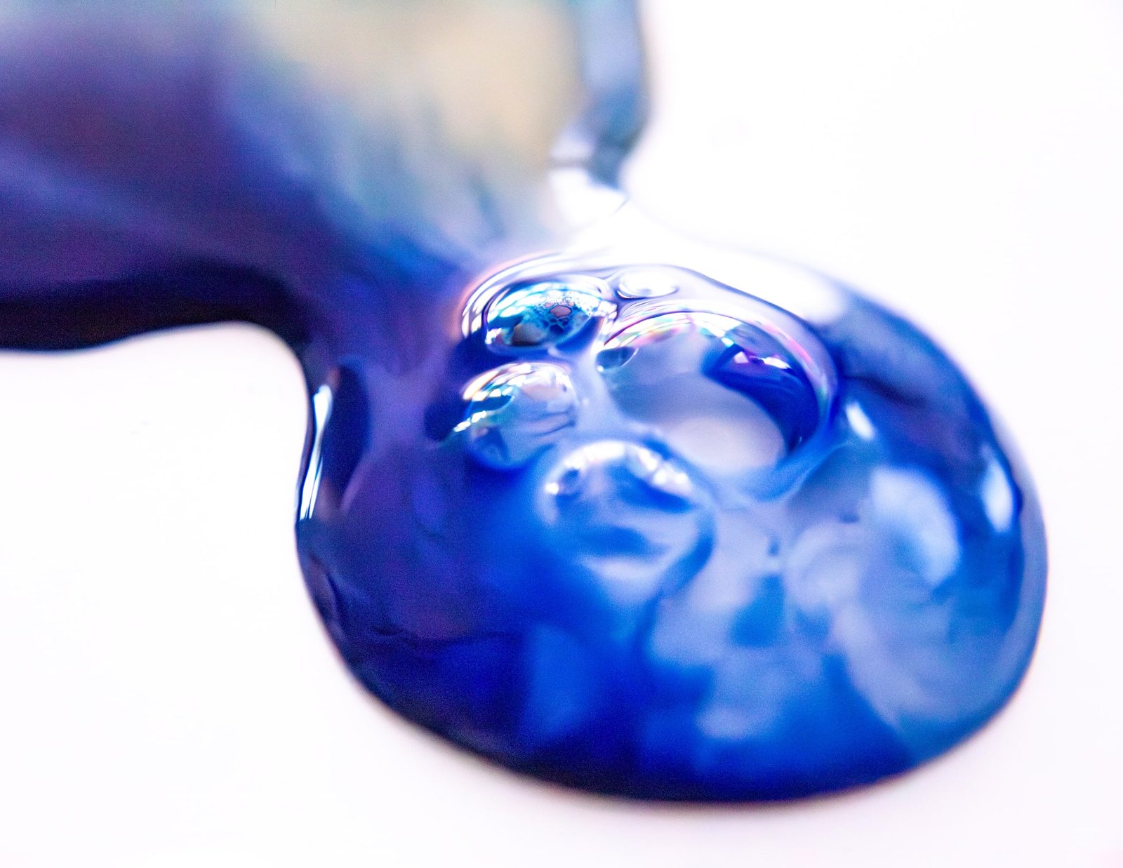 A glossy pool of deep blue paint with clustered bubbles on a white ground.