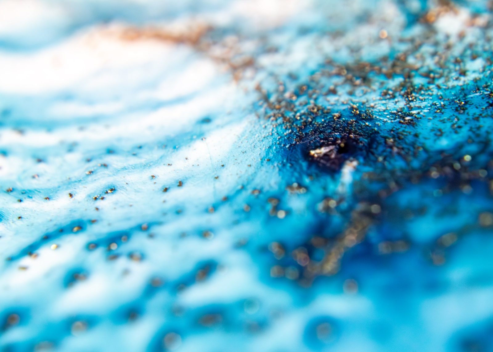 Turquoise bubbly texture surrounding a pale cloud-like centre, with a cluster of gold flecks.