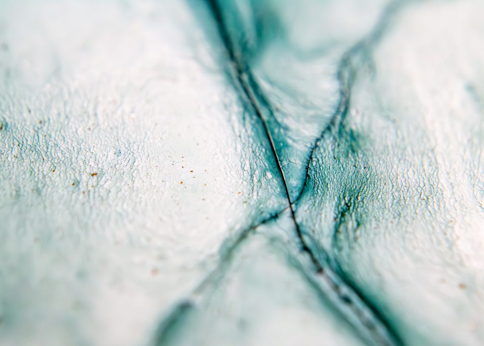 Teal fracture lines crossing in an X against a pale mottled ground.