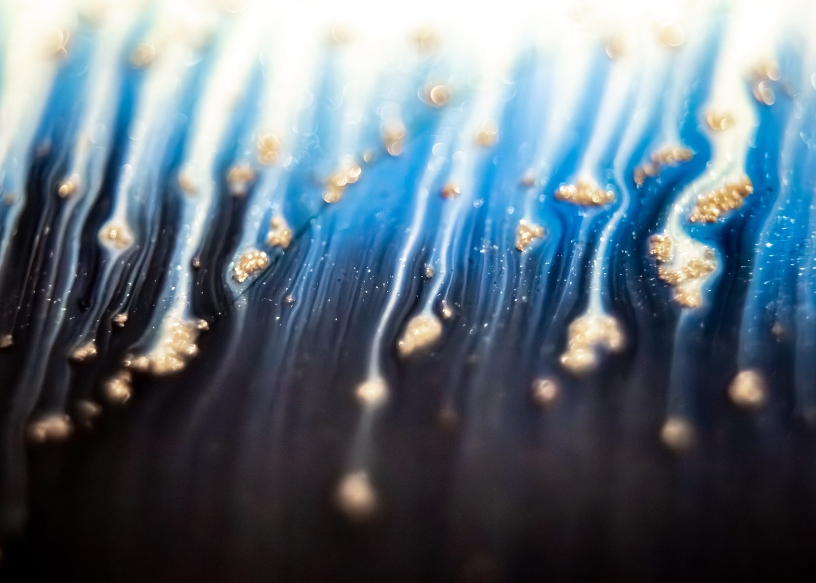 Indigo rivulets streaming downward through black, dotted with small gold specks.