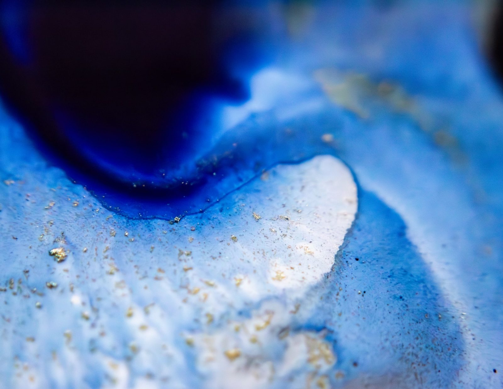 Deep blue pooling ink with a dark indigo plume and scattered gold flecks.