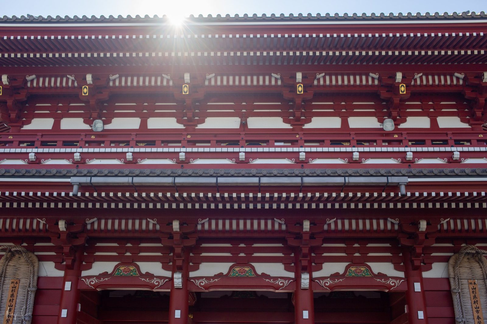 Sun flaring over the tiered red and white eaves of a temple building