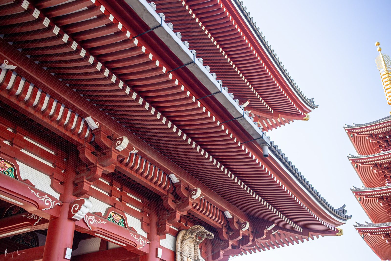 Layered red temple roof eaves against blue sky with a pagoda beyond