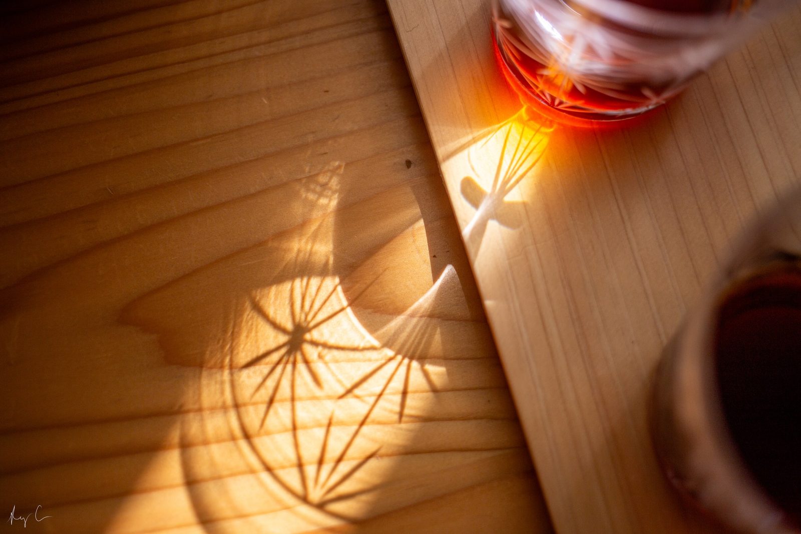Starburst light patterns cast on a wooden table beside glasses of amber drink