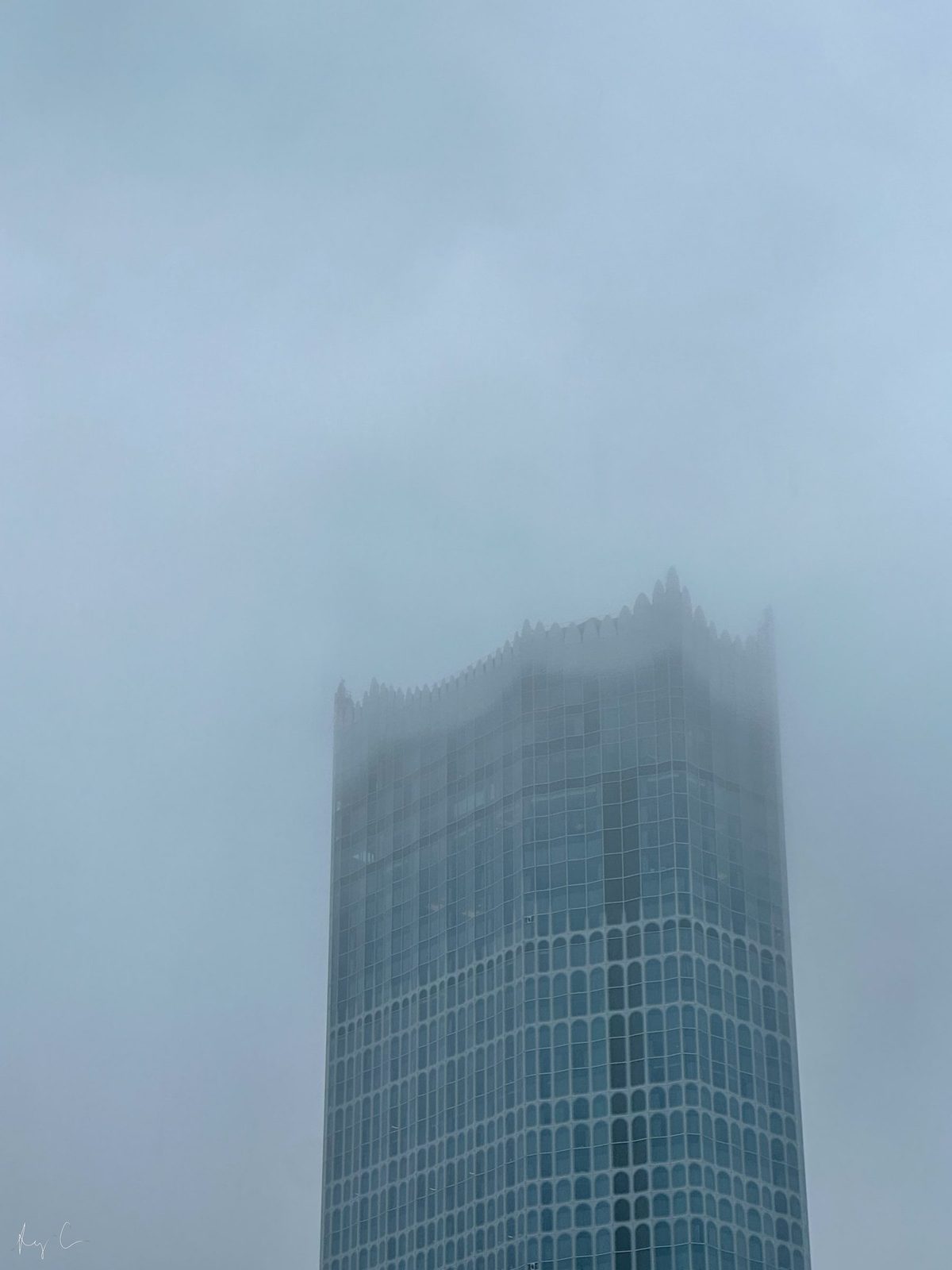 Top of a tall glass skyscraper with its crown obscured by low cloud