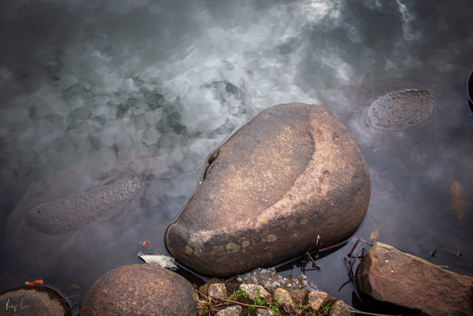 Smooth rounded rocks partly submerged in still cloud-reflecting water