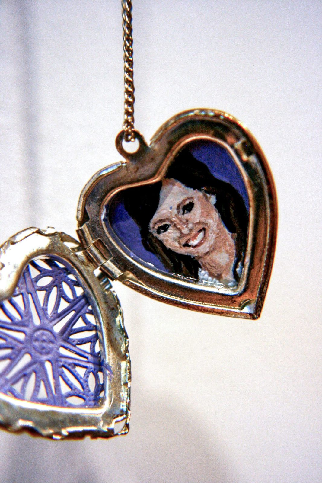 Open gold heart-shaped locket with blue enamel interior, holding a painted portrait of a smiling dark-haired woman.