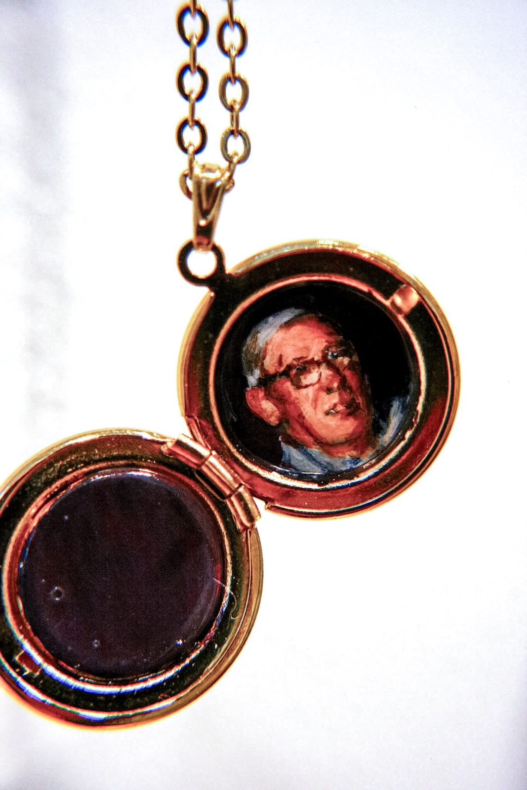 Open gold round locket holding a painted portrait of a man wearing glasses.