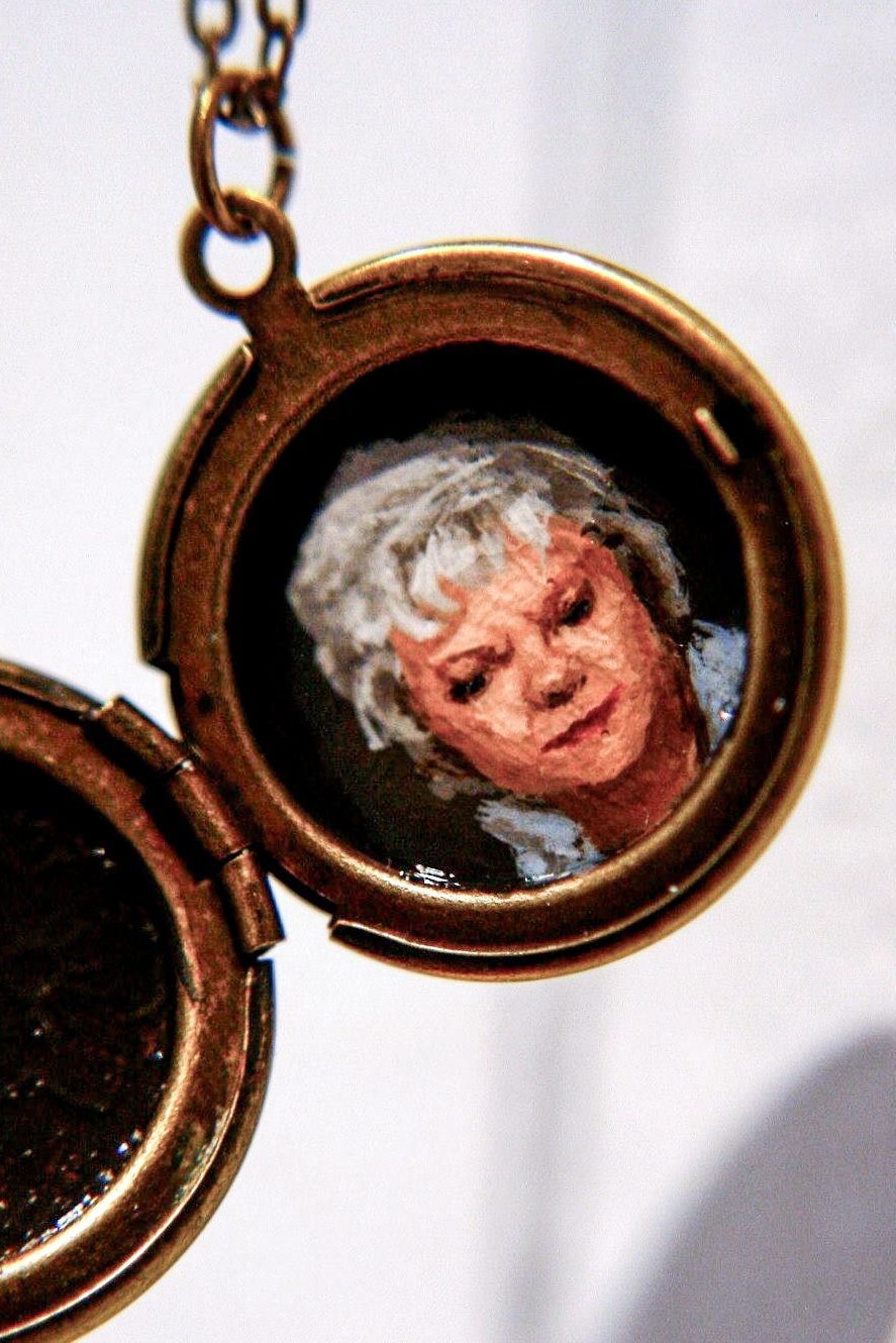 Open bronze round locket holding a painted portrait of a woman with curly white hair.