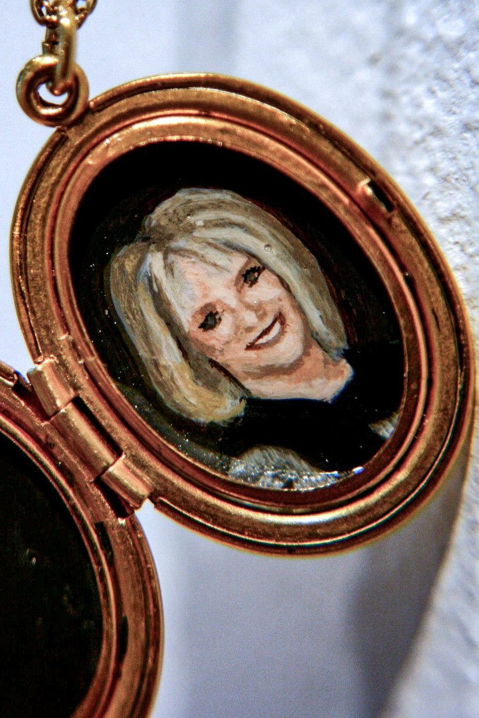 Open gold oval locket holding a painted portrait of a smiling blonde woman.